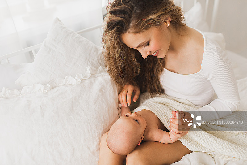 漂亮的年轻妈妈和她可爱的新生儿在床上玩耍。图片素材