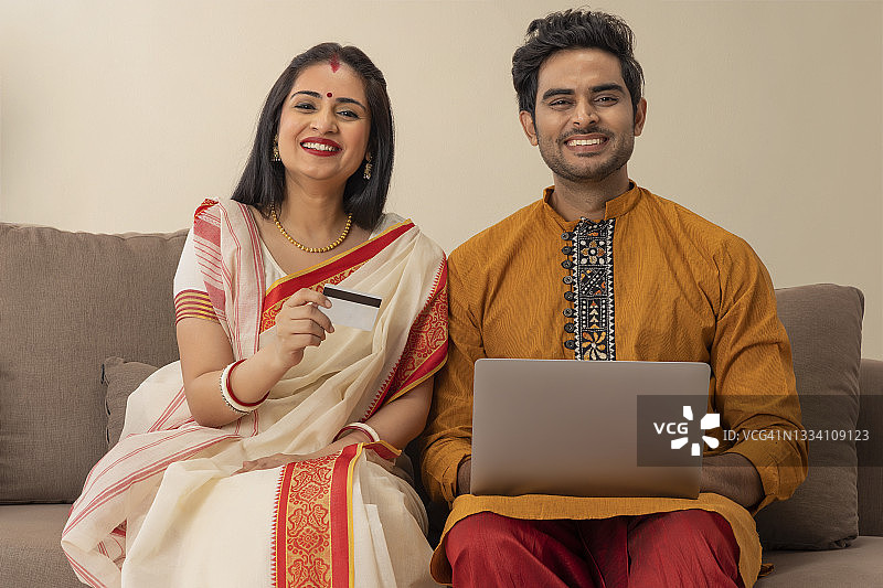 一对穿着传统服装的年轻夫妇坐在家里进行网上交易图片素材