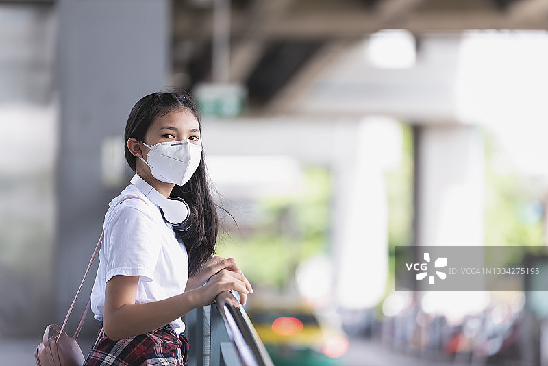 在冠状病毒大流行期间，一名亚洲年轻女子戴着口罩站在公共场所，以预防户外传染病。基本的设备来保证我们新生命的安全。图片素材