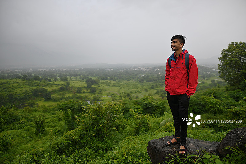一个年轻人站在山谷边缘的一块岩石上看风景图片素材