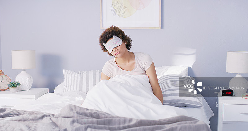 一个女人坐在床上，戴着她的睡眠面具图片素材