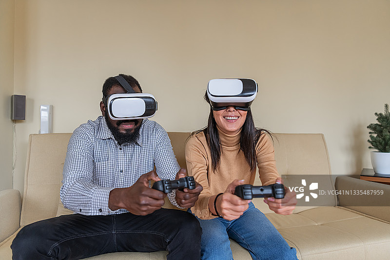英俊的非洲人和他的亚洲女友正在用虚拟现实模拟器玩电子游戏。图片素材