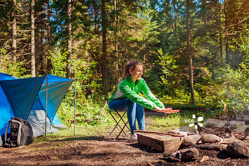 在森林里的营火旁休息的女人坐在帐篷旁温暖的手。夏季露营。独自旅行图片素材