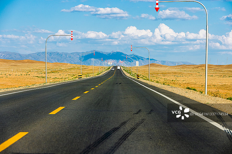 沿着戈壁沙漠，笔直的道路通向远方。路边的箭头引导正确的车道。中国新疆维吾尔自治区。图片素材