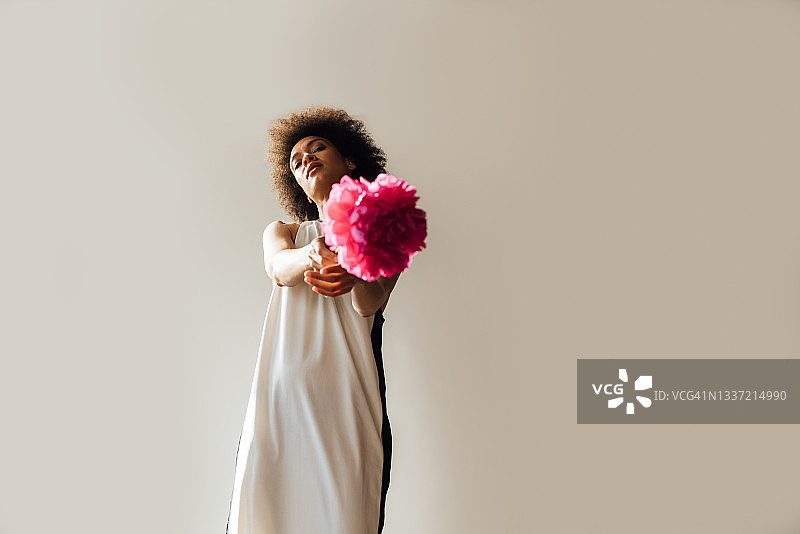 一名美丽的非洲裔美国妇女将粉色裁剪的花朵指向相机的水平镜头(被捕捉到的运动)图片素材