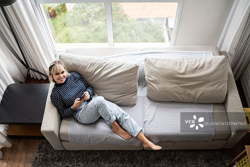 一位中年女性坐在家里的沙发上使用智能手机的高角度照片图片素材