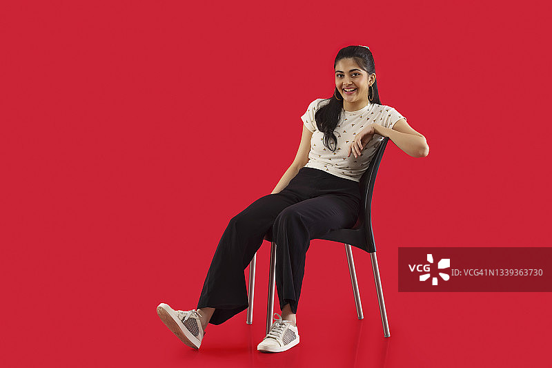 一张坐在红色背景椅子上的年轻女子的肖像。图片素材