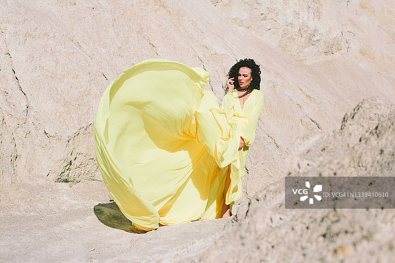 一名年轻女子站在采石场的岸边，靠近沙地，身穿黄色夏装，对着镜头摆姿势图片素材