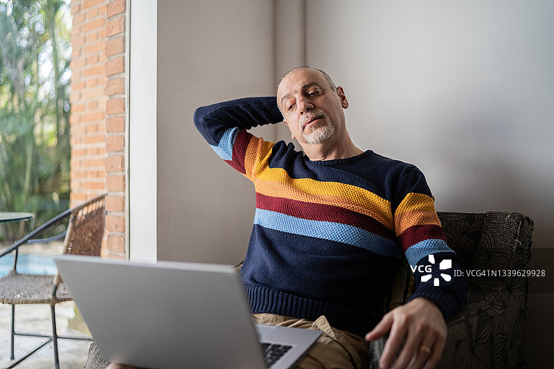 一个成熟的男人坐在家里摆弄笔记本电脑的时候伸着脖子图片素材