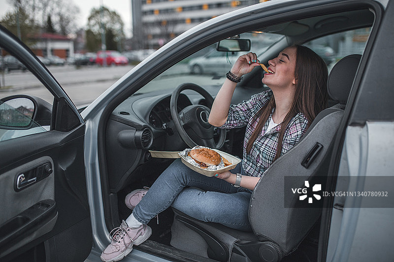 年轻女司机在停车场吃不健康食品图片素材
