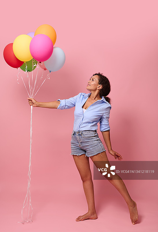 全长身体大小，迷人的惊人的愉快的高兴的卷发混合种族非洲女士手持一束空气球企业活动组织派送孤立的粉红色背景图片素材