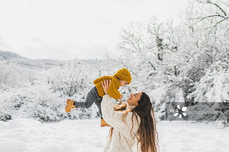 年轻漂亮的母亲和女儿在雪外的森林里玩耍。和谐的家庭图片素材