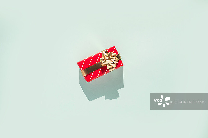 礼盒与白红色条纹图案和金色蝴蝶结在浅蓝色背景与阴影。平铺风格和特写图片素材