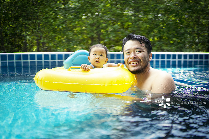 亚洲年轻的父亲感受着积极的情感和享受，首先带着女儿在游泳池上的黄色游泳圈为宝宝的家庭生活理念图片素材