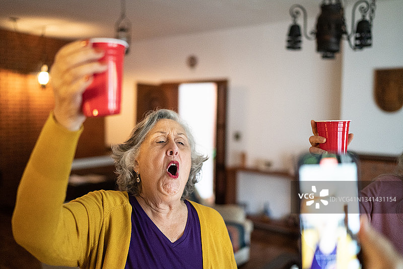在家中聚会时，一位年长的女性被人用智能手机拍摄或拍照图片素材
