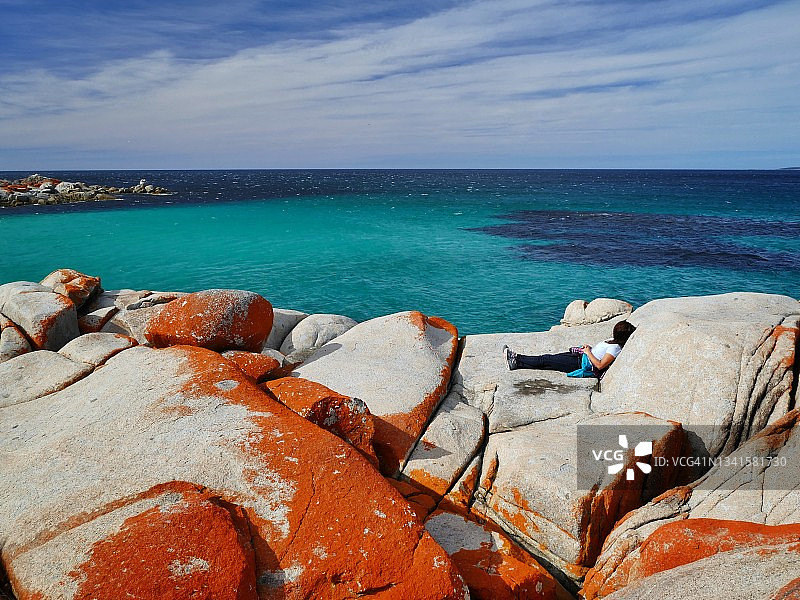 澳大利亚塔斯马尼亚州比纳龙湾附近，一名女子在蓝色海面上的岩石上放松图片素材