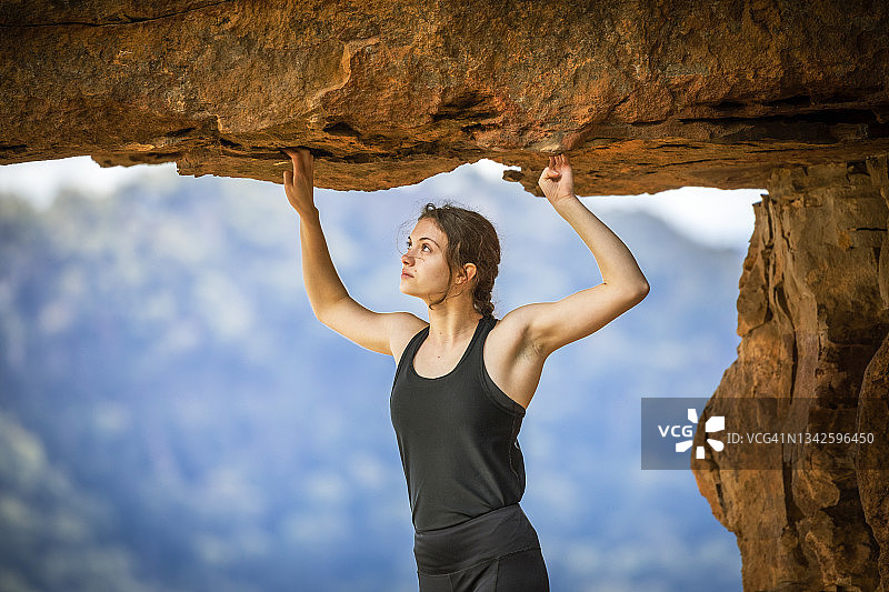 女子岩石攀登者举起手臂，手持悬崖岩石悬，山图片素材