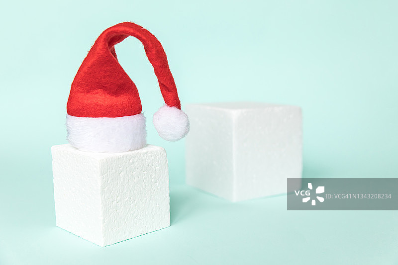 简单的最小组成冬季物体圣诞老人帽子和立方体形状的几何形式讲台孤立的蓝色粉彩背景。圣诞节新年概念为12月时间。空间模型,复制图片素材