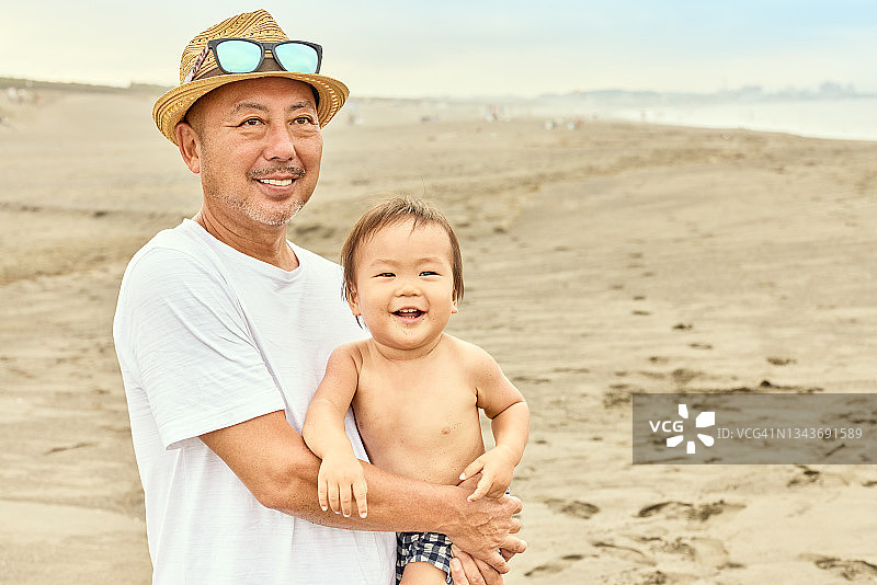 一幅婴儿在海滩上被父亲拥抱的肖像。图片素材