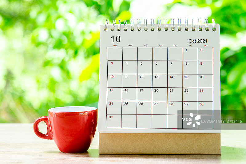 十月月，2021年日历桌，供组织者规划和提醒木制桌子，红色杯咖啡与绿色自然背景。图片素材