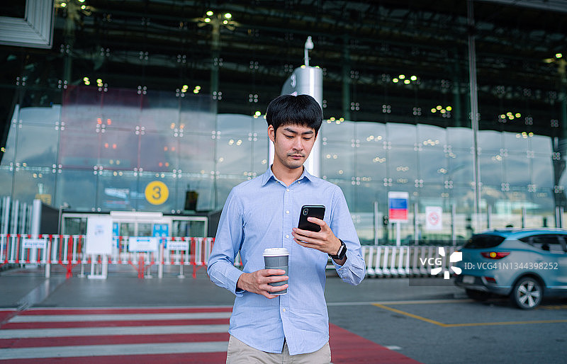 年轻的亚洲男性在国际机场大厅里用智能手机查看时间图片素材