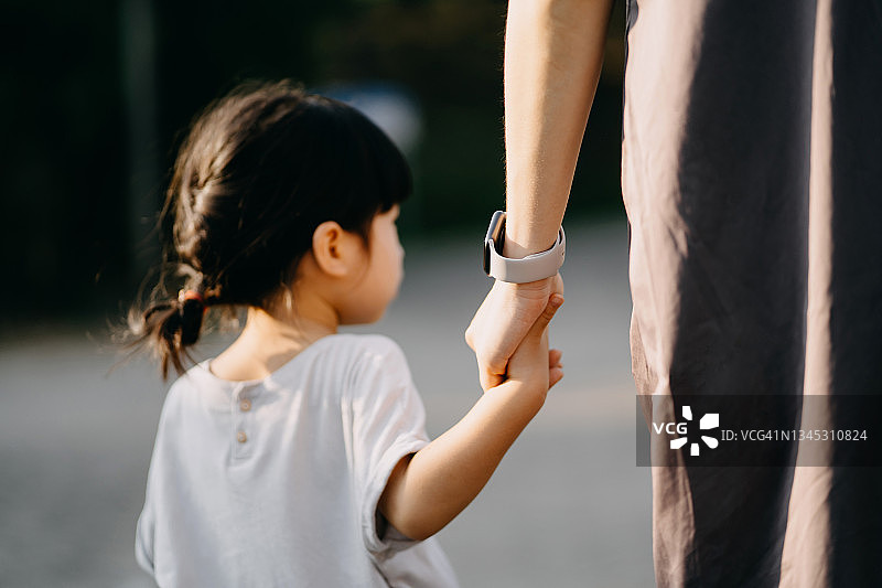 后视图，靠近年轻的亚洲母亲与她的小女儿手牵手散步，享受家庭纽带时间在公园日落。亲情与关怀图片素材