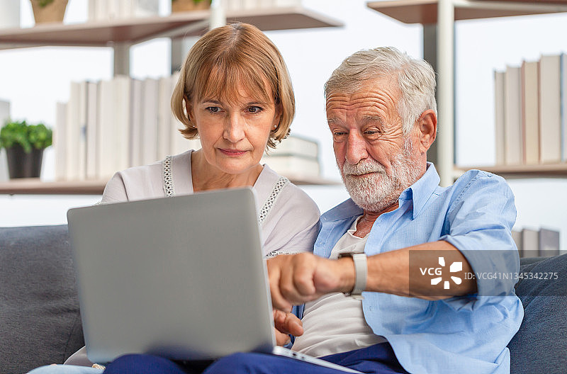 幸福的老夫妇在客厅的肖像，老女人和一个男人在舒适的沙发上使用电脑笔记本电脑，幸福的家庭概念图片素材