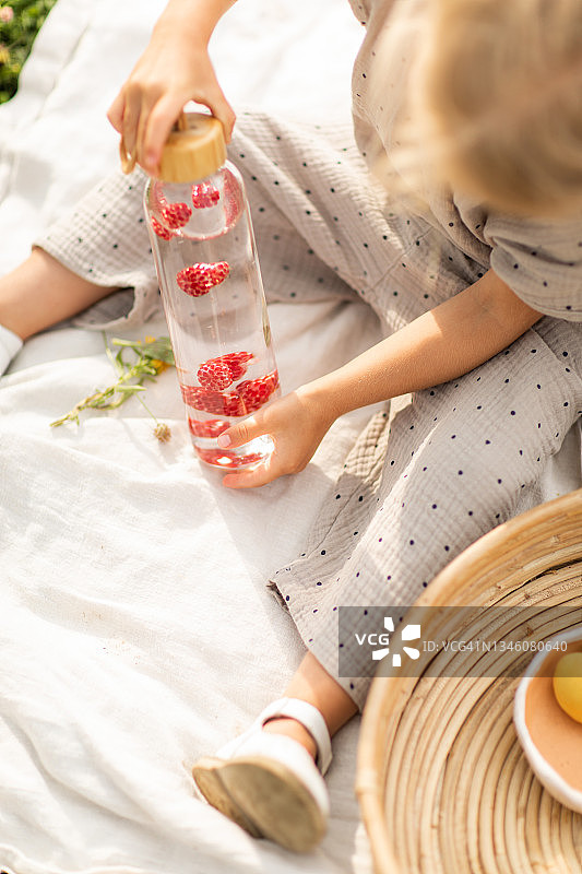 夏日户外野餐，小女孩的手拿着装有草莓的玻璃瓶。图片素材