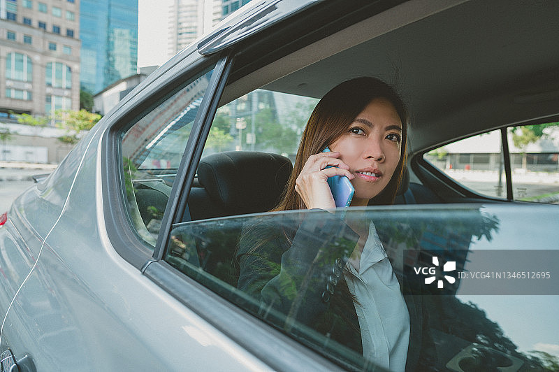 美丽的亚洲女商人正在汽车后座上用智能手机聊天图片素材