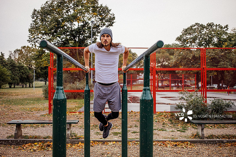 秋天下雨天，一群穿着灰色运动服的年轻人在公园里用健身器材锻炼图片素材