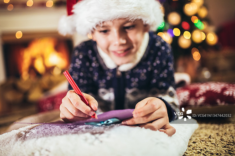 男孩在圣诞树旁给戴着红帽子的圣诞老人写信图片素材