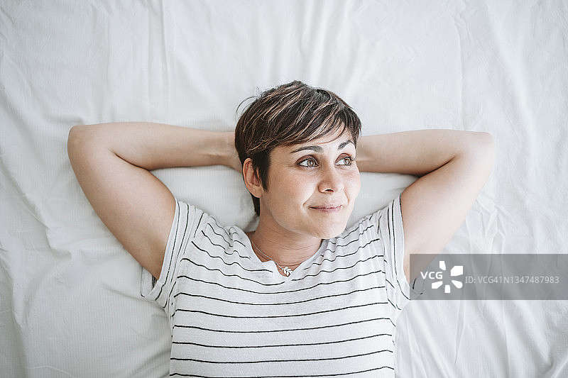 一个体贴的女人双手放在脑后躺在家里的床上图片素材