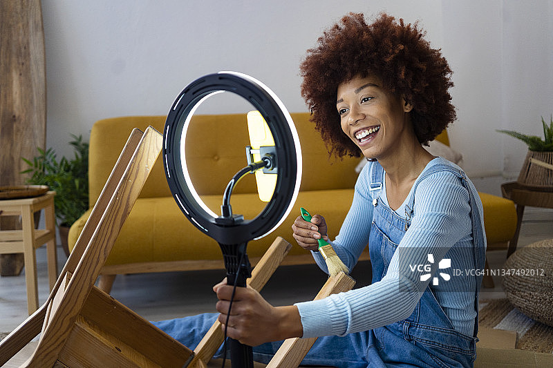 一个非洲女人一边在家用智能手机发视频，一边在椅子上作画图片素材