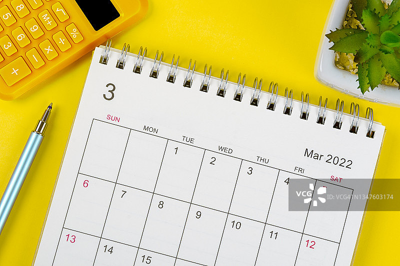 日历桌2022年3月月，顶部视图日历组织者计划和笔，计算器，室内植物的黄色背景。图片素材
