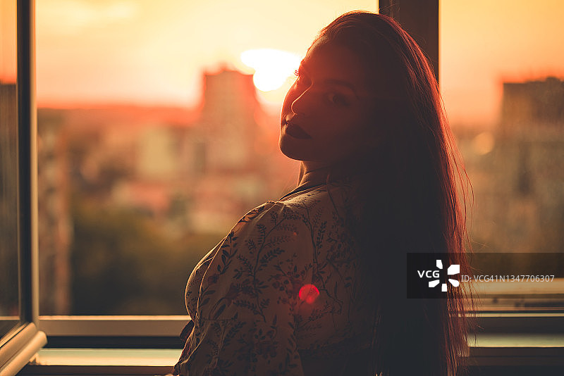 日落时分，美丽的女人站在窗前图片素材