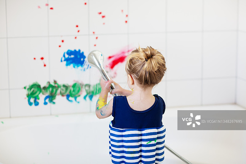 蹒跚学步的男孩在用手指画完后正在清洁浴室的墙壁图片素材