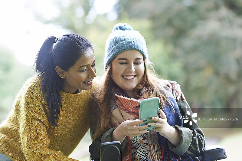 一位残疾妇女和朋友在秋天公园使用手机。图片素材