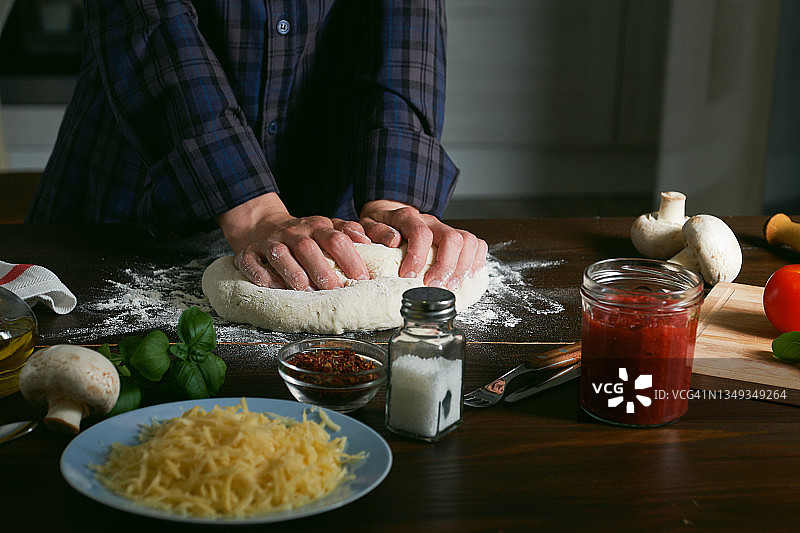 用蔬菜，番茄酱，奶酪和蘑菇在家烹饪意大利素食披萨，在木制厨房桌子上。一个女人，厨师或管家用她的手揉和卷面团。家庭生活。一步一步的指导，自己做。步骤1。图片素材