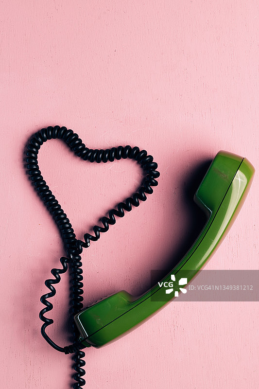 复古的绿色拨号电话喇叭与电缆在一个心形。用爱沟通的概念。图片素材