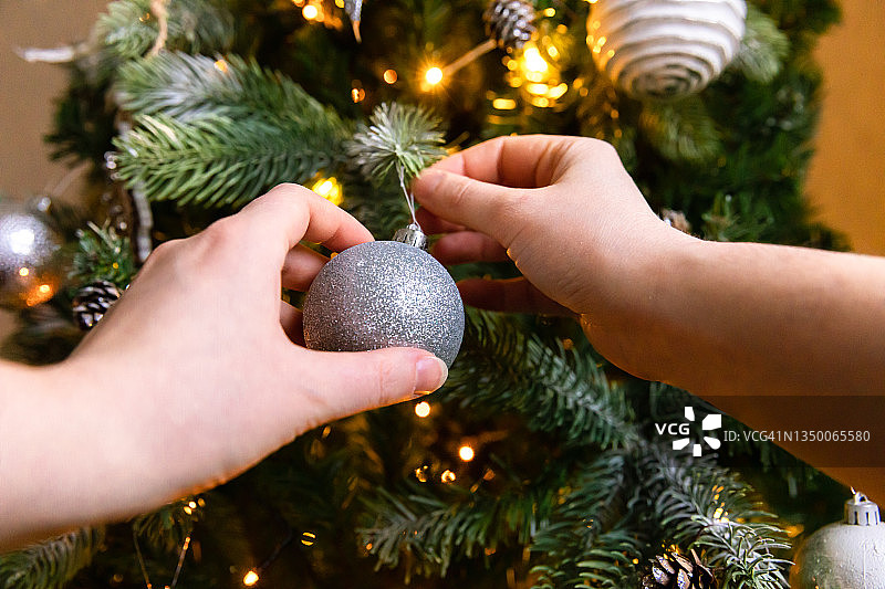 女人用手装饰圣诞树。圣诞树有白色和银色的装饰，装饰玩具和球。现代古典风格的室内设计。平安夜在家，该庆祝了图片素材