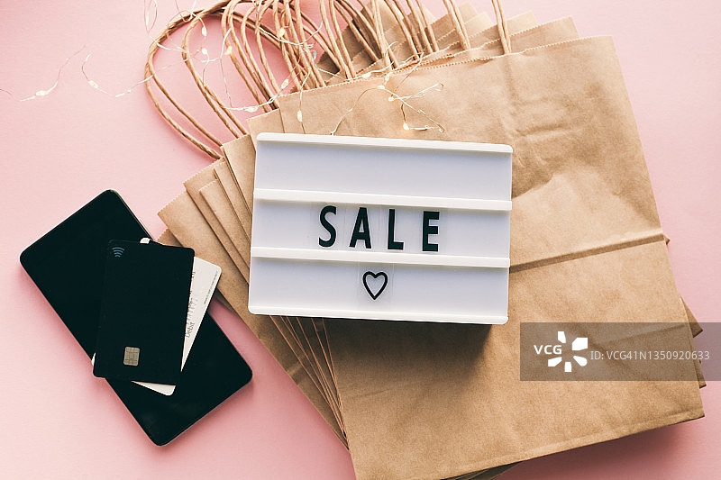 纸购物袋，电话和支付卡和灯箱销售在粉红色的背景。促销和黑色星期五的概念。图片素材