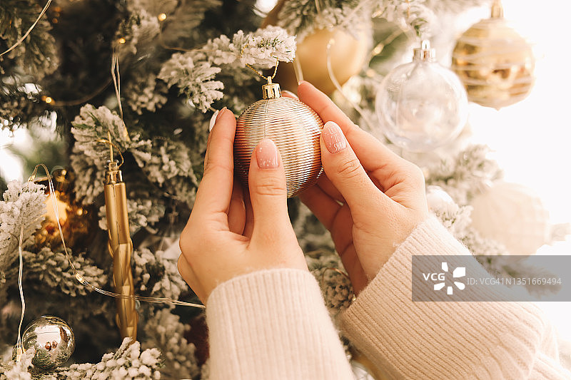 女人的手修得很好，穿着舒适的毛衣，正在为圣诞节做准备，用气球和玩具装饰圣诞树，打开新年家里的节日礼品盒图片素材