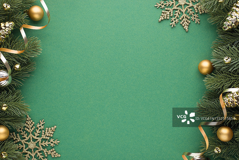 俯视图照片的金色和银色的圣诞树球玩具锥，小铃铛，雪花和蛇在松树树枝上孤立的绿色背景与空的空间图片素材