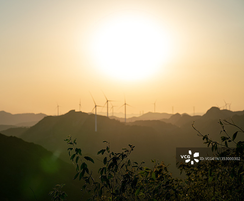 日落时的植物和远处山上的风力涡轮机图片素材