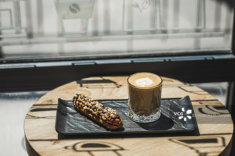 坚果巧克力泡芙和黑盘子上的一杯白咖啡。美丽的阳光照在桌子上图片素材