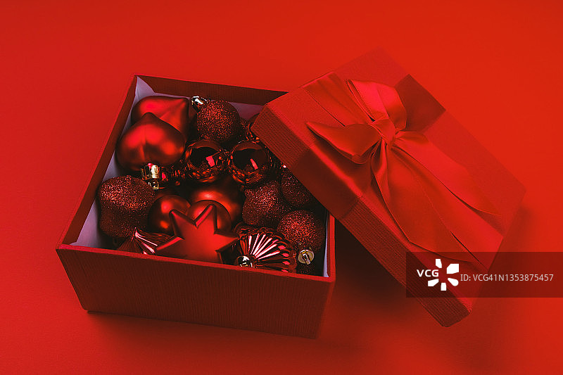 打开红色的礼盒，大蝴蝶结和红色背景下发光的圣诞玩具。图片素材
