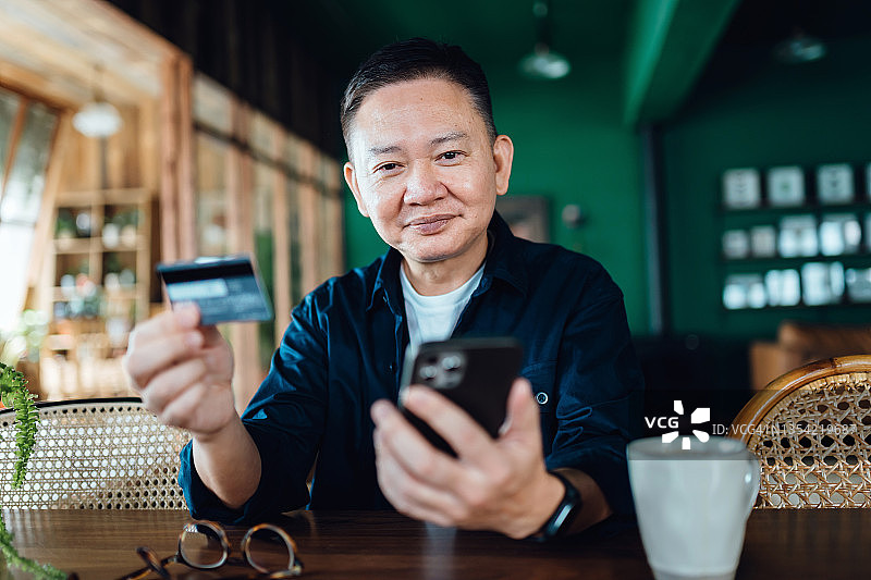 亚洲高级男子在家里用智能手机在线购物，用信用卡在线支付。网上购物，网上银行。老年人和技术图片素材