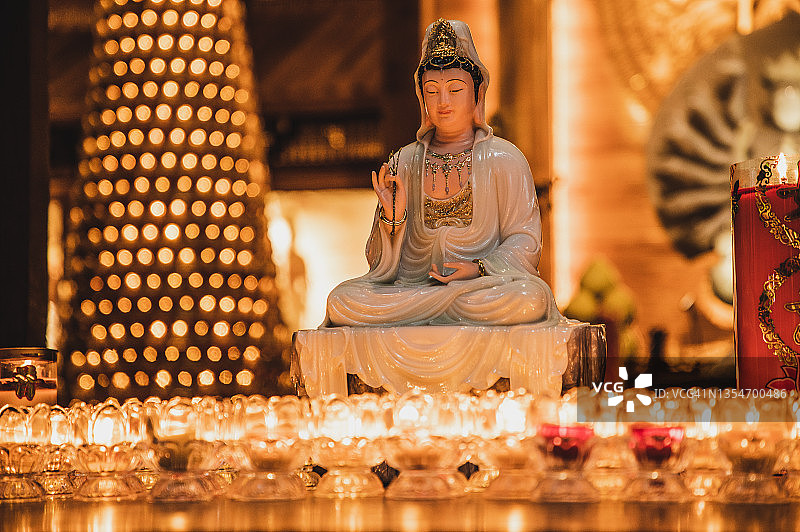 一座佛教寺庙里的观音菩萨像，桌上放着许多点燃的祈祷蜡烛图片素材