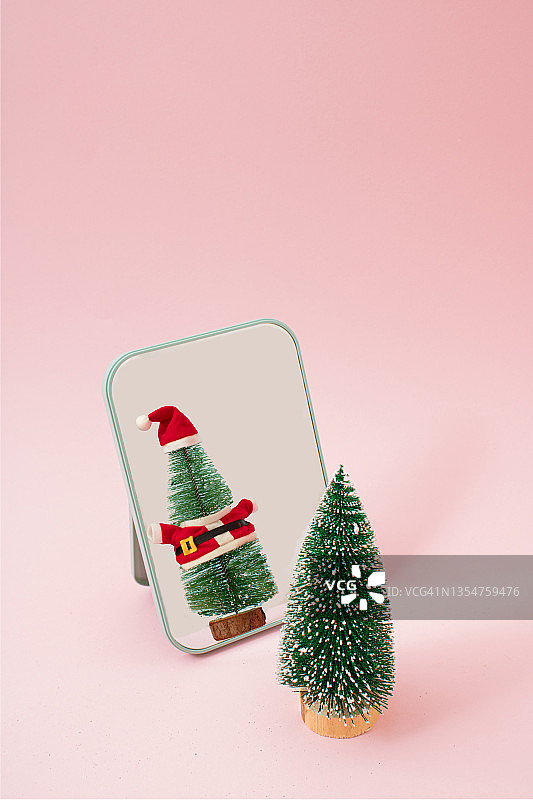 圣诞树在镜子里打扮成圣诞老人在粉红色的蜡笔背景。圣诞和新年背景最小假日设计和概念图片素材