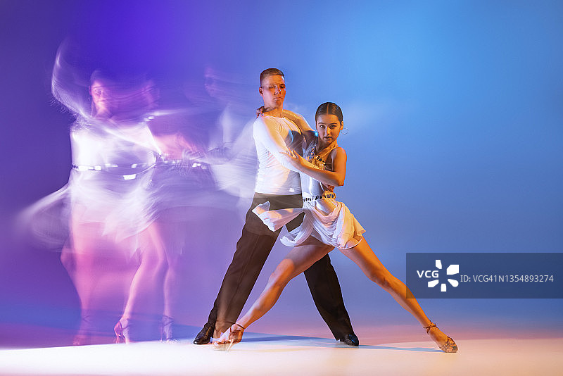 动态肖像舞者，灵活的男人和女人跳舞交际舞孤立在梯度蓝紫色背景下霓虹混合光图片素材